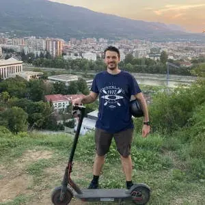 Matt standing next to his Xiaomi M365 Pro electric scooter and holding an electric scooter helmet